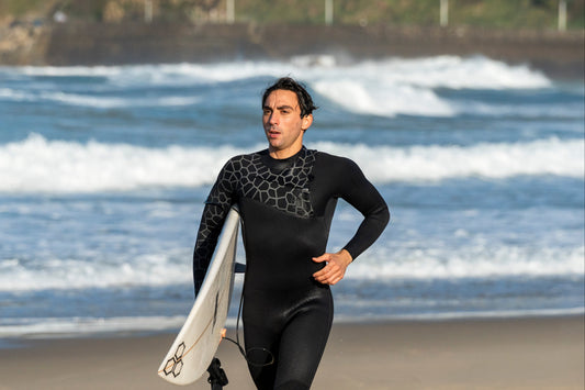 Person in a wetsuit running on a beach with a surfboard
